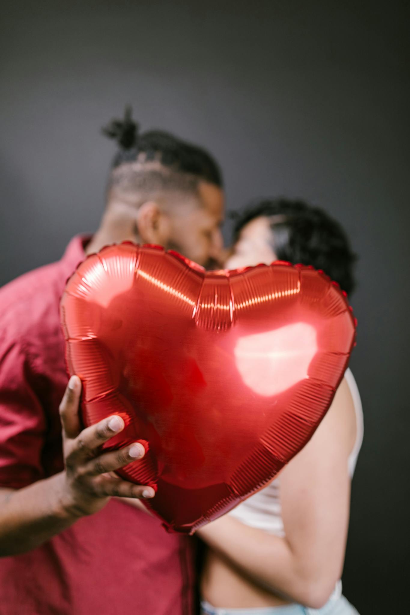 A couple sharing an intimate moment with a heart-shaped balloon, symbolizing love and romance.